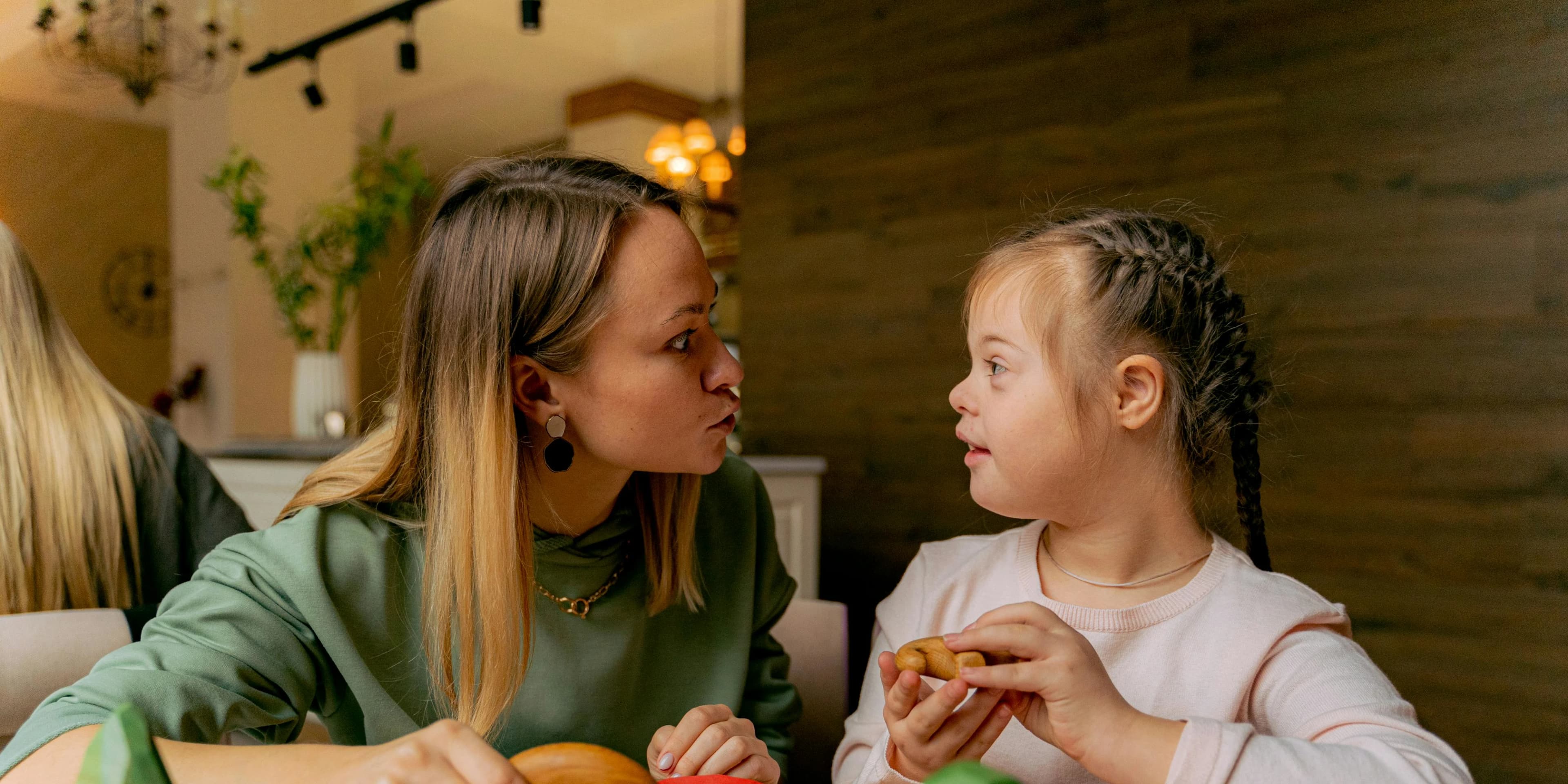 Downs syndrome girl playing with caregiver in doors at table with toys